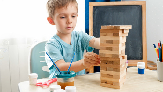 聪明的男孩从由砖头制成的高塔上拉木块聪明的儿童概念和在封闭孤立期间的家庭教育概念聪明的男孩将木块从由砖头制成的高塔上拉出来聪明的背景图片