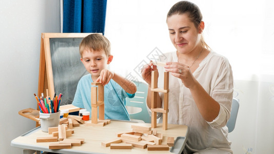 年轻母亲与小儿子玩耍在客厅用木块和砖头在桌边玩耍用木块和砖头在桌子上玩耍聪明孩子的概念和在被禁闭自我孤立期间的家庭教育养和教学年背景图片