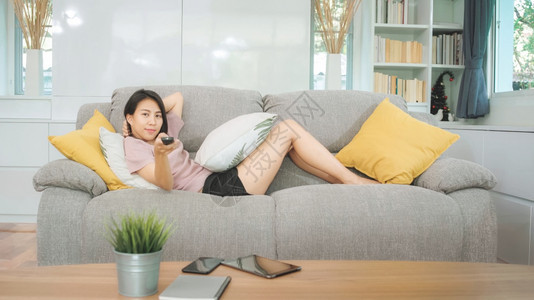 年轻亚洲少女在家看电视客厅沙发上躺着女感到快乐图片