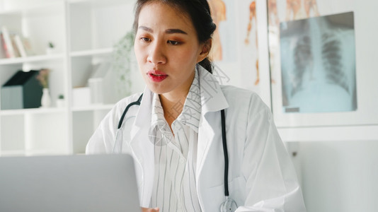 白制服听诊器的亚洲年轻女医生使用电脑笔记本交谈视频话在诊所或医院的服务台与病人通话图片