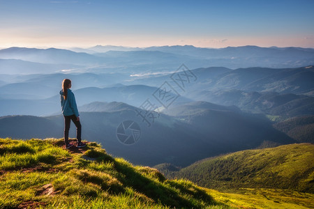 山顶上的女孩绿色草地看着美丽的山谷夏天日落时雾中风景与运动的年轻女子雾山森林天空旅行和游远足背景图片