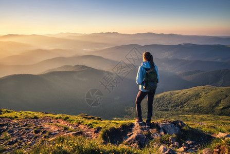 山顶上的女孩绿色草地看着美丽的山谷夏天日落时雾中风景与运动的年轻女子雾山森林天空旅行和游远足背景图片