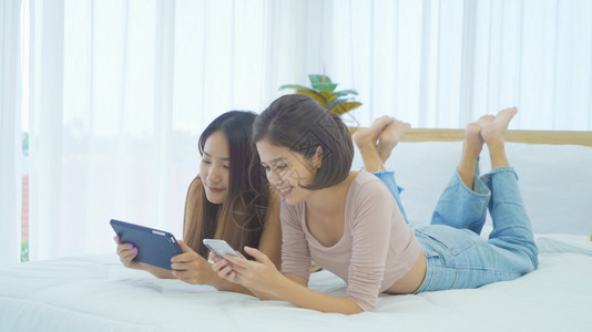 快乐的亚洲女青年孩躺在床上,家中卧室看平板电脑,学习技术设备概念。图片
