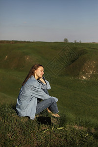 年轻女坐在青草山上夏天阳光明媚的日子感到轻松图片