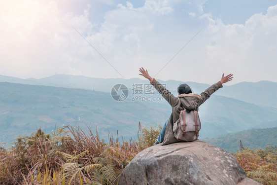 穿着背着包的坐在山顶岩石上与天空的蓝色相对图片