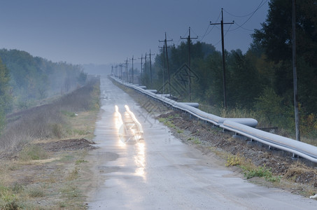 汽车在清晨沿管道阴云模糊的木材沥青公路上行驶铁轨铺在树林中路两侧经过一条输电线图片