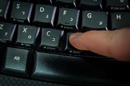 用希伯来语和英字母在无线键盘上打字的人按粘贴钮顶视图黑暗气氛图片