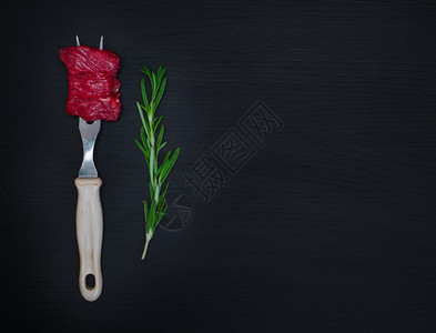 铁制厨房叉子上的肉片和黑木背景上的玫瑰绿枝右侧空位图片