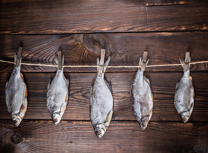5个咸鱼头挂在一根绳子上挂在棕色木背上图片