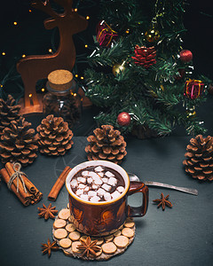 巧克力加棉花糖棕色杯子的棉花糖黑色背景在圣诞节装饰品后面图片