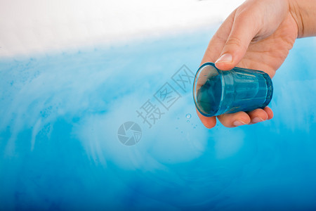 手握着从蓝色玻璃中倒下的水图片