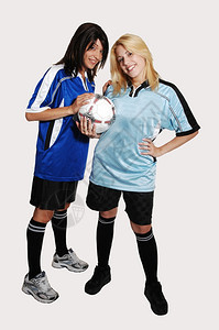 两个年轻漂亮的女足球员拿着穿俱乐部的制服站在工作室里寻找浅灰色背景图片