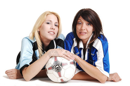 身着制服的两名年轻女足球员躺在地板上一个工作室里带着一个足球白色背景图片