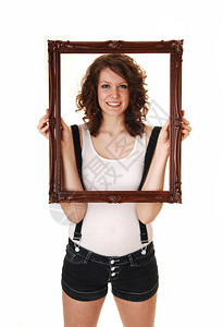 一个穿牛仔裤的年轻美女穿着吊带和白色T恤在工作室里拿着一个图片框白色背景背景图片