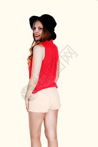 一个可爱的年轻女子穿着短裤和帽子站在背后孤立的白种背景图片
