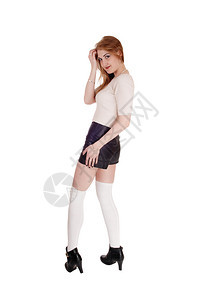 一个年轻可爱的黑发美女站在白色背景黑皮短裤长的白袜和高跟鞋图片