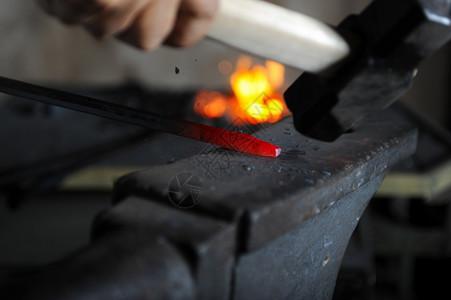 铁匠在铁炉里锻造一个烧红的铁高清图片
