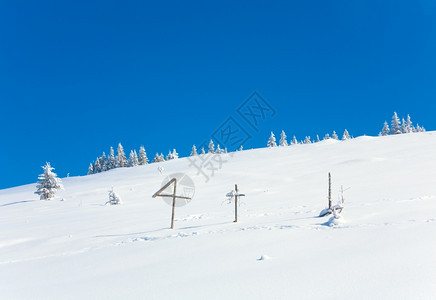 山边蓝天空背景和前面木十字的山坡上冬季雪壁树喀尔巴阡山乌克兰图片