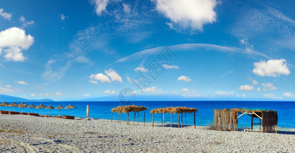 夏晨沙滩,有防晒床、树冠和白石块(阿尔巴尼亚伯什),深蓝天空有云层三缝全景。图片