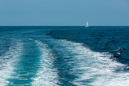 海上的快艇或渡轮尾巴和远处的白帆船自然和假期背景图片