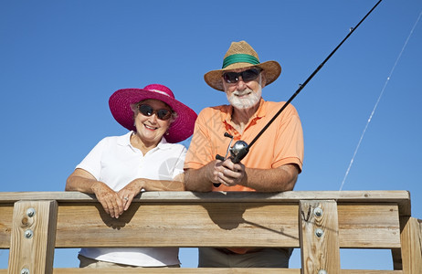 老年夫妇在钓鱼戴帽子和墨镜时保护自己免受太阳的照射图片