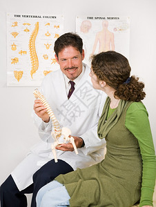 友善的微笑脊椎按摩师使用模型向病人解释脊椎神经系统图片