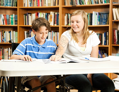 在学校图书馆辅导年轻残疾男孩的少女图片
