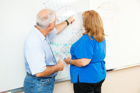 成人教育学生在老师的帮助下在董事会上做数学方程式工作学习高清图片素材