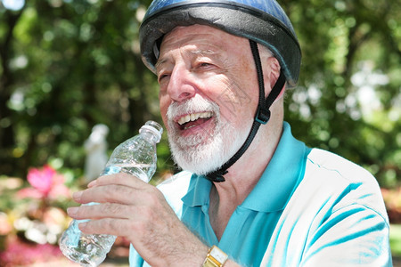 身着自行车头盔的活跃老人停下来喝瓶装水图片