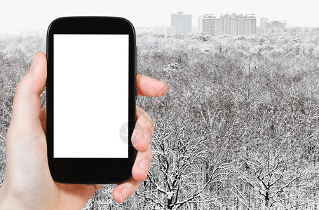 旅行概念手持智能机在背景上剪出屏幕下雪森林和城市图片