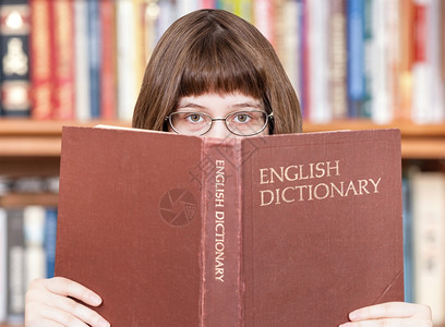 有眼镜的女孩看英语词典书本和背景架图片