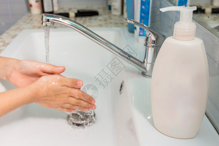 儿童在水龙头下洗手在前景一管液肥皂图片