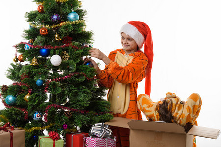 一个女孩把球挂在圣诞树上另一个女孩带着头爬进盒子里图片