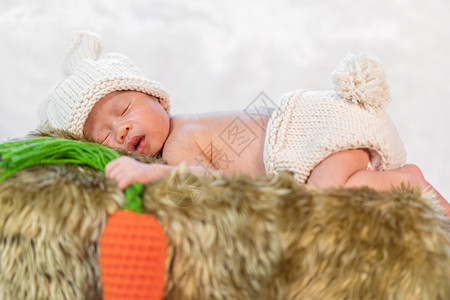 穿着衣服兔子穿着兔子服装的新生儿婴睡在毛皮床上背景