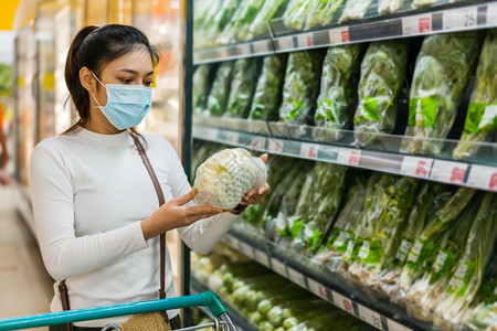 年轻妇女在超市购物时选择蔬菜并戴着预防冠状新冠大流行病的医疗面具图片