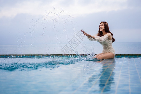在有海背景的游泳池里玩水年轻女子图片