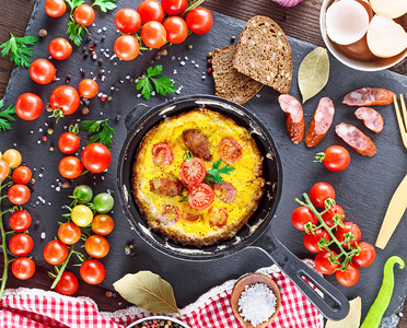 鸡蛋炸煎红樱桃西番茄香肠在蔬菜中间的餐桌上黑煎锅里图片