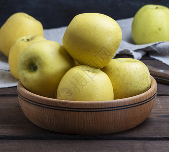 满的黄苹果放在桌上的木碗里图片