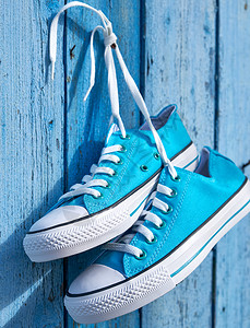 一对蓝色的纺织运动鞋挂在墙上的钉子旧破碎木板有选择焦点图片