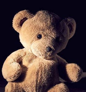 老棕色泰迪熊坐着石膏粘在前额上黑色背景图片
