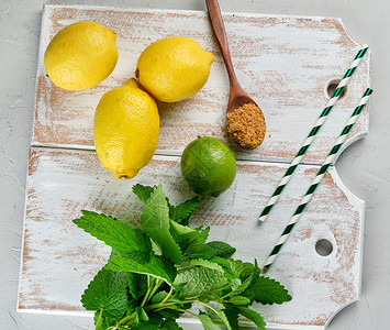 黄熟的全柠檬和棕糖白木板上一串新鲜薄荷顶层风景柠檬水的原料图片