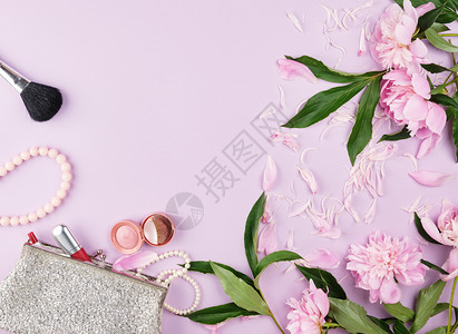 彩红口亮光阴影和手镯的银女化妆袋由珍珠和一束花朵罗马制成放在紫色面纸顶视图复制空间的紫色面画背景上图片