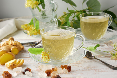 茶杯透明来自姜和叶子在白木板上旁边的糖块和树枝绿色的叶子图片