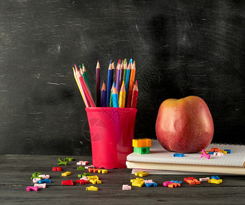 在一堆笔记本上成熟的红苹果在空黑粉笔板背景上用红色文具玻璃和多木铅笔回到学校概念图片