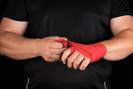 健身包运动员身着黑色衣服在训练前用红色纺织弹绷带包着双手黑背景在训练前用红色纺织弹绷带包起来背景