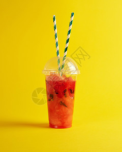 在一个塑料杯中用成熟的红西瓜制冰雪黄底两根纸管背景图片