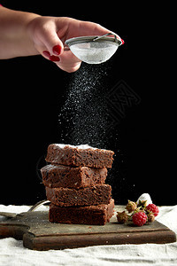 堆成的正方面包巧克力蛋糕切片从铁筛子上洒白糖小粒子飞下来低键图片