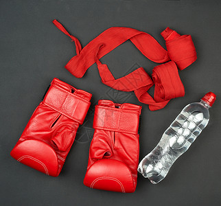 一对红色皮革拳击手套捆绑运动员手的纺织品绷带黑底的瓶水顶视平铺图片