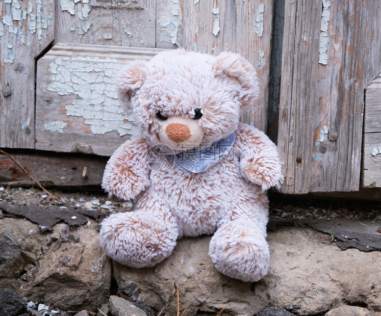 小泰迪熊坐在门口靠近一扇旧门漆破的关上图片