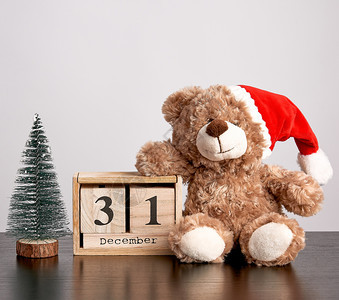 红帽子的棕色泰迪熊日期为12月3日的桌木历和绿色装饰树圣诞背景图片
